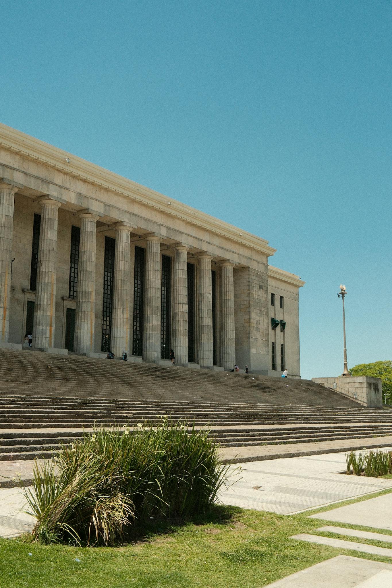 A grand neoclassical building featuring pillars under a bright blue sky.