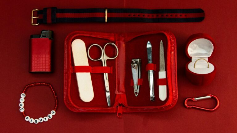 Flat lay of a red manicure kit with fashion accessories on a matching backdrop.
