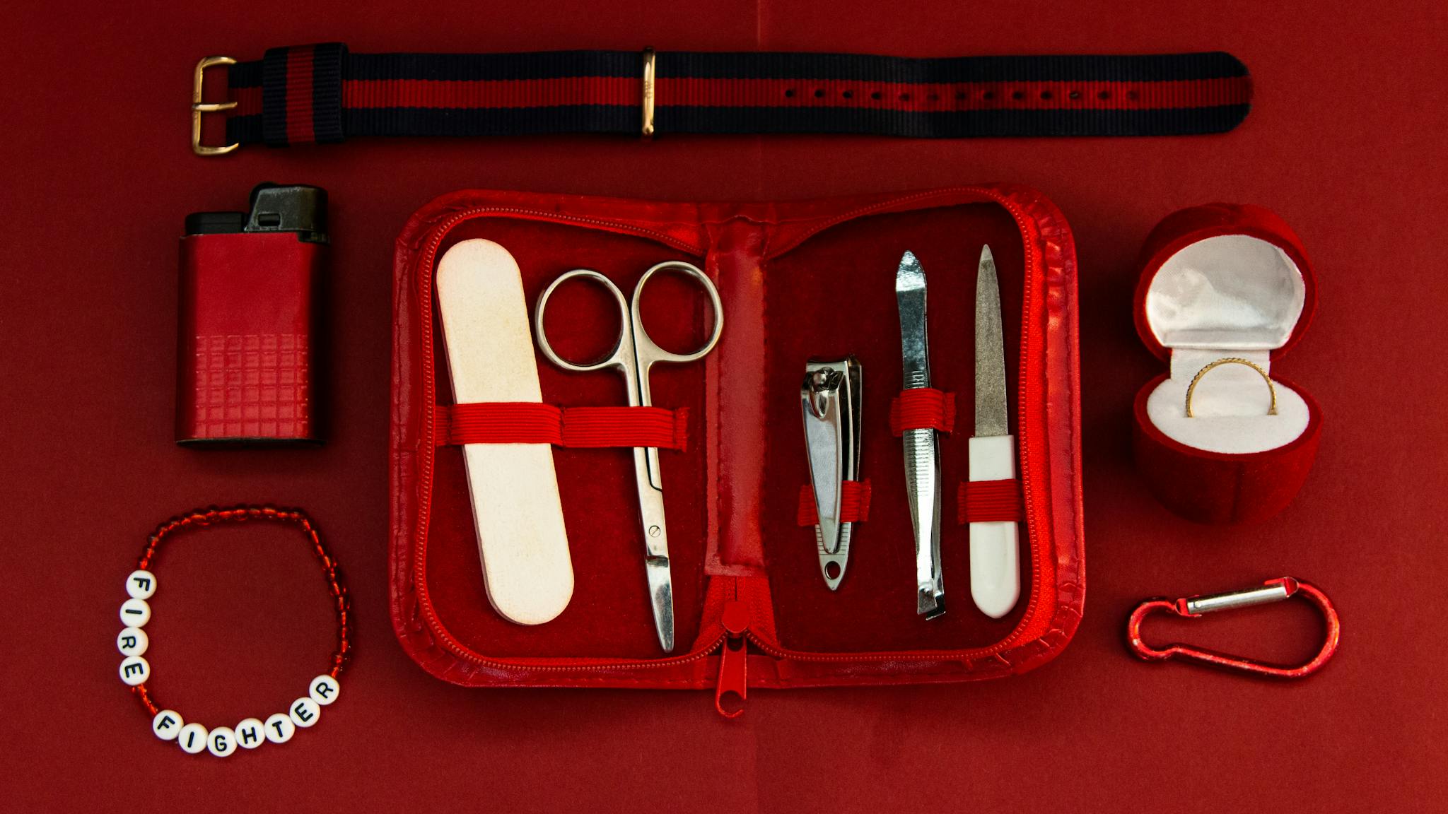 Flat lay of a red manicure kit with fashion accessories on a matching backdrop.
