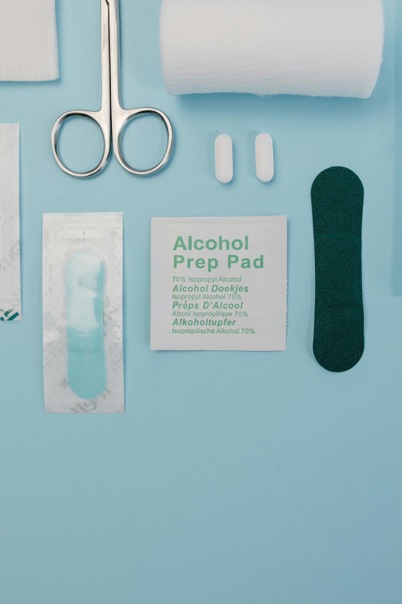 Top view of medical supplies including gauze, scissors, and alcohol prep pad on blue background.